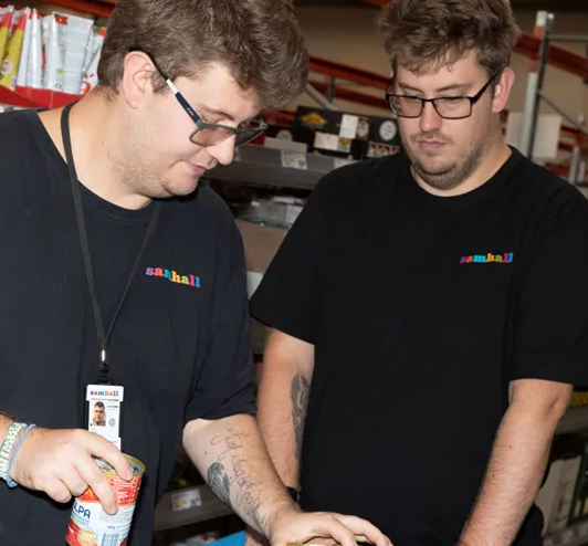 Två Samhallmedarbetare arbetar tillsammans i en butiksmiljö och hanterar varor.