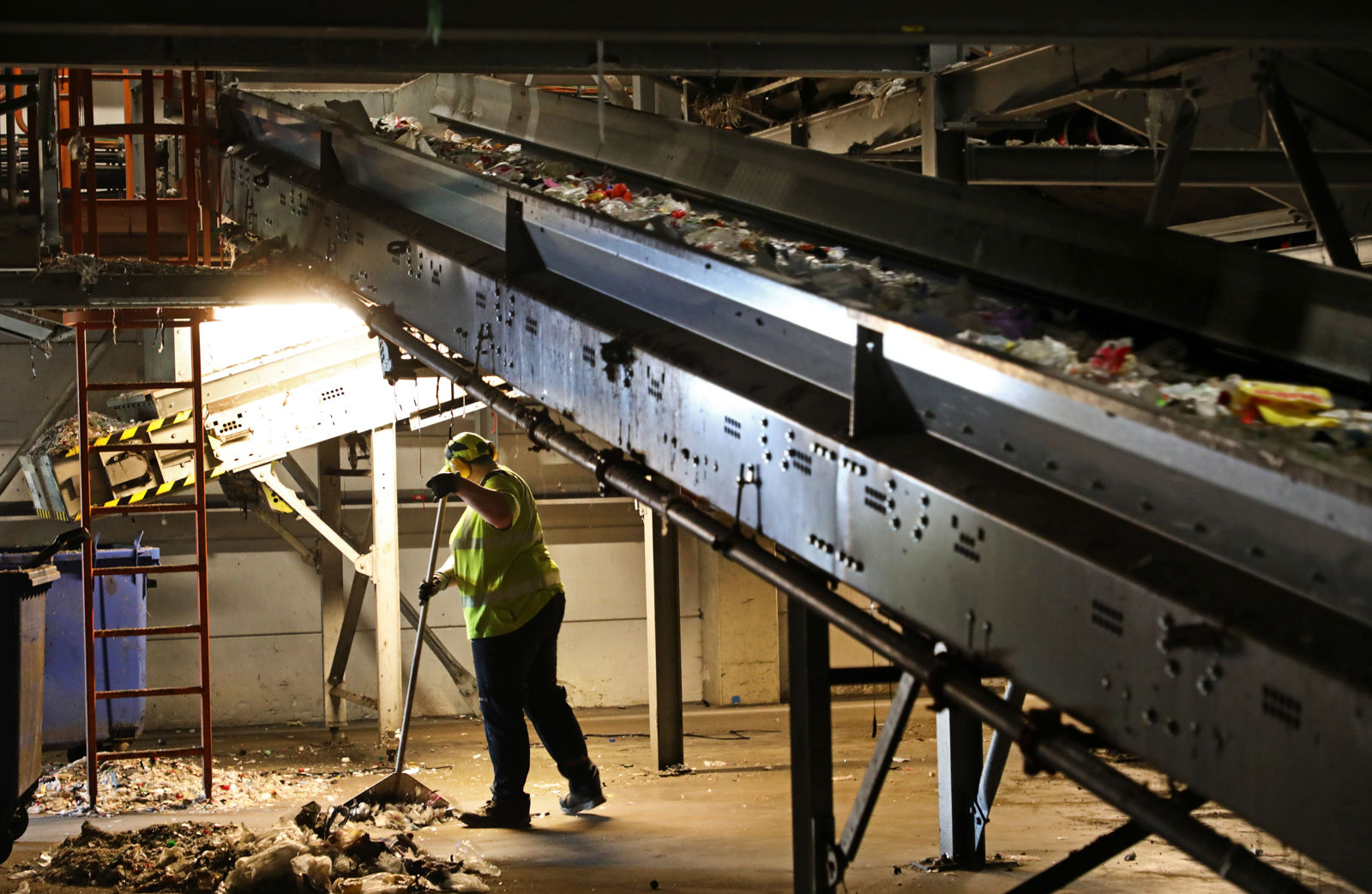 Samhallsmedarbetare arbetar med städning under ett transportband i en industrimiljö.