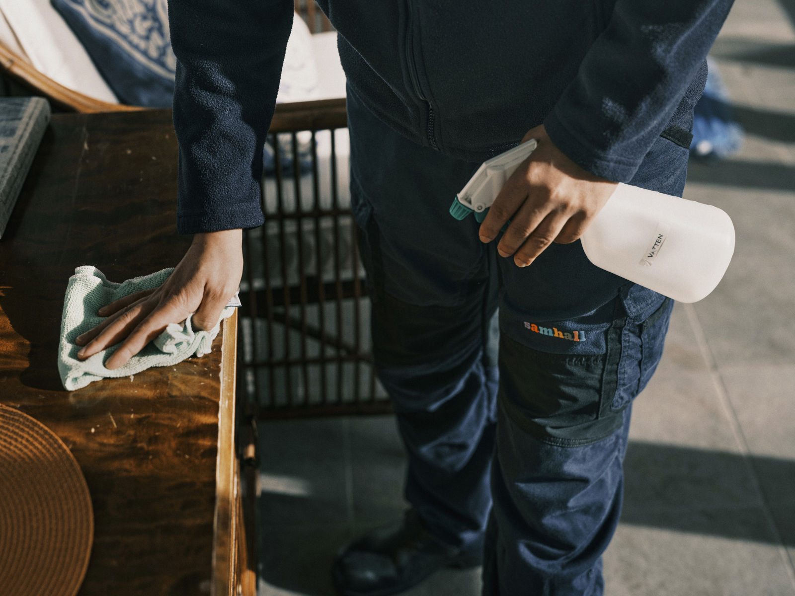 Person torkar av ett bord med trasa och håller en sprayflaska i handen.