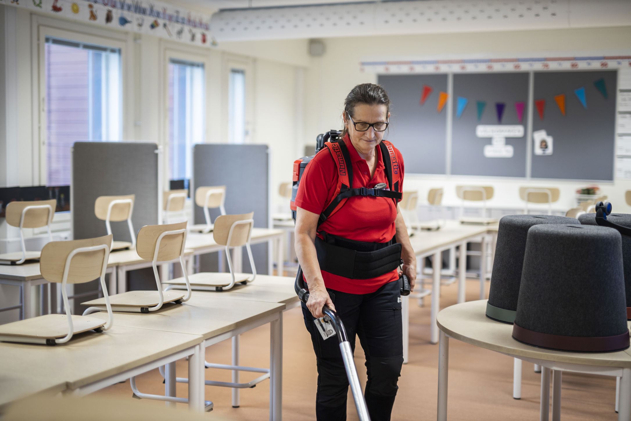 En Samhallmedarbetare dammsuger ett klassrum där stolarna är uppställda på borden efter skoldagen.