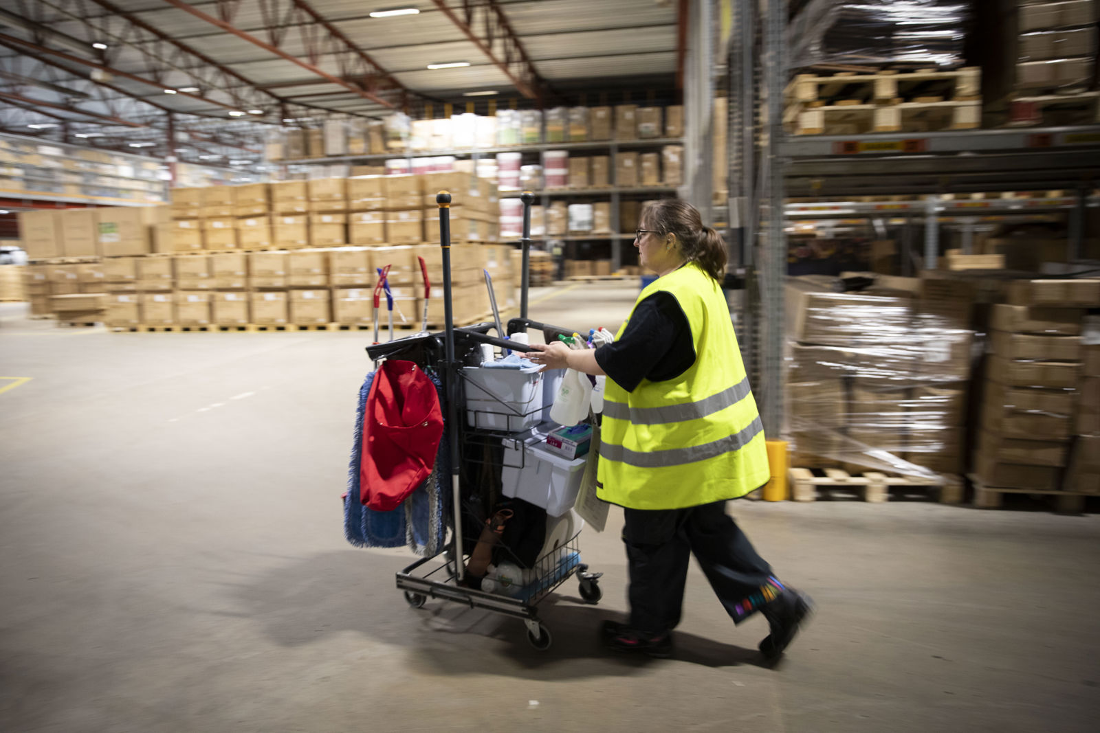 En samhalls-anställd i en lagerlokal som skjuter på en tvätt vagn.