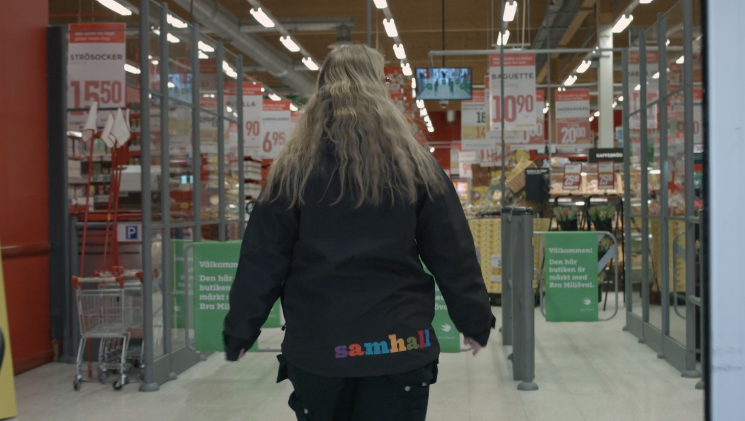 En kvinna med långt hår går längs gången i en butik.