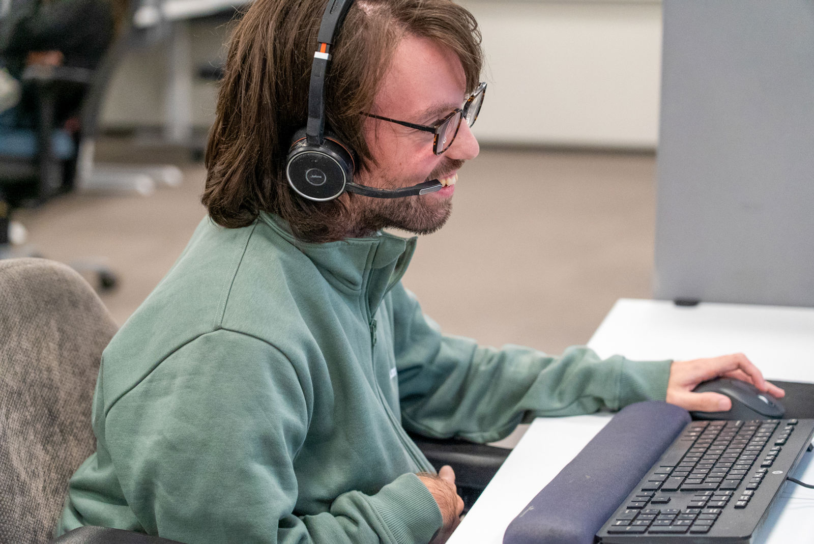 Person med headset sitter vid en dator och arbetar i kontorsmiljö.