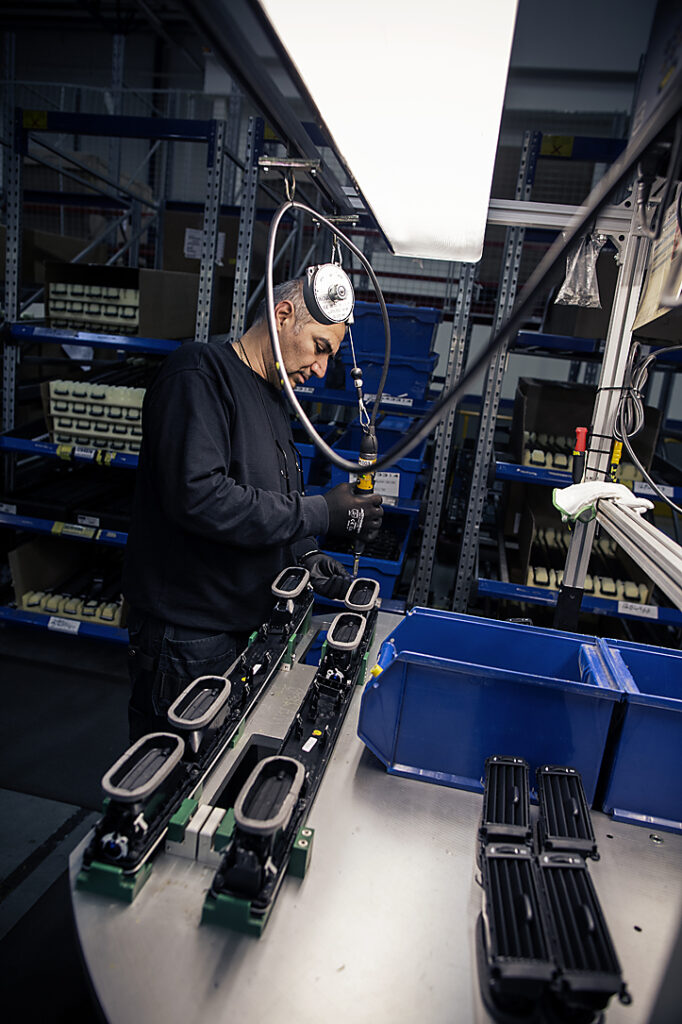 Samhallsmedarbetare monterar komponenter vid en arbetsstation i industrimiljö.