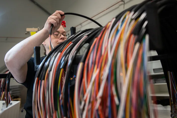 Carina arbetar med de stora kablarna som hänger på en ställning. Det är färgglada kablar. 