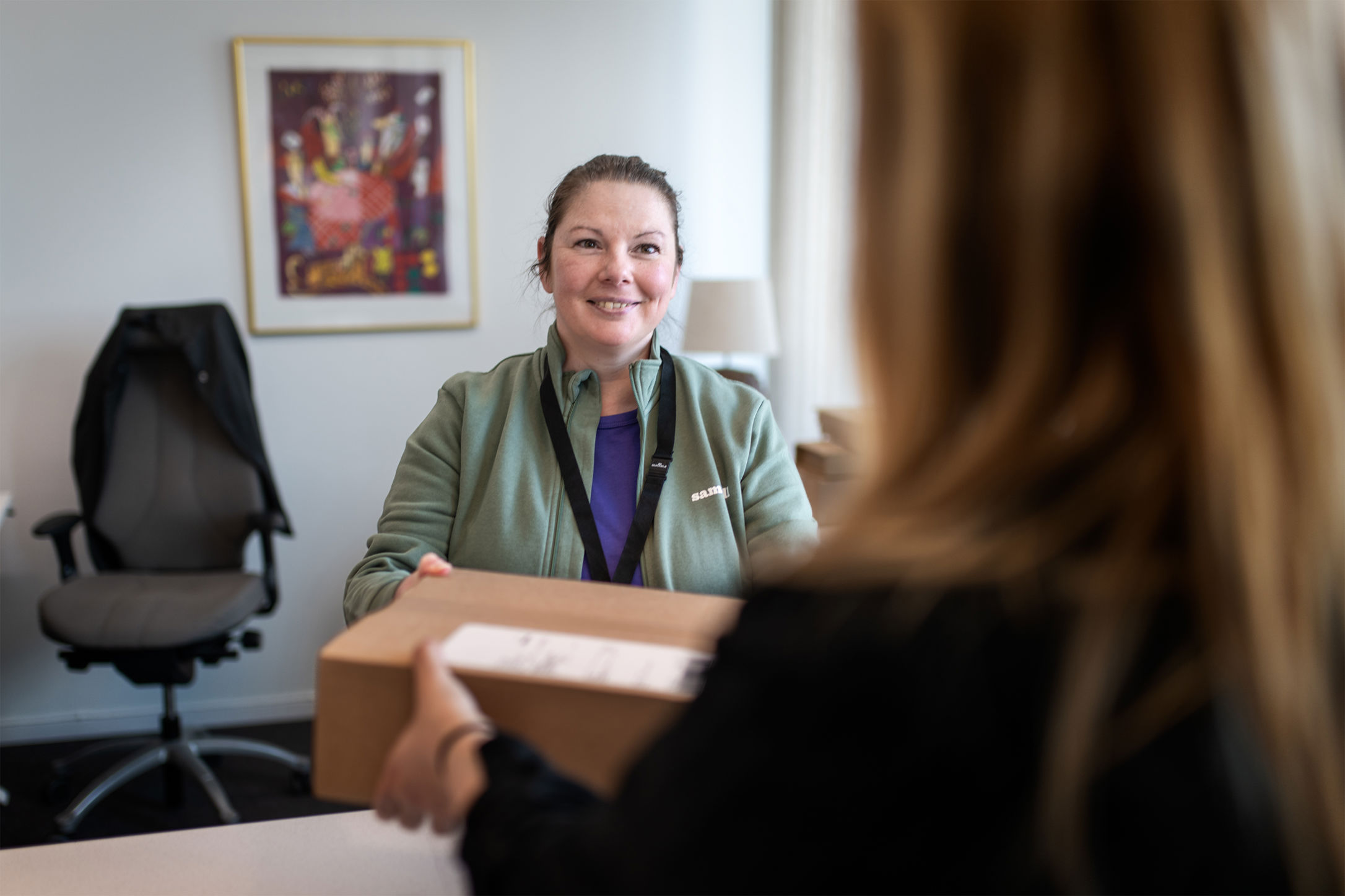 En Samhallmedarbetare tar emot ett paket från en kund i en kontorsmiljö.