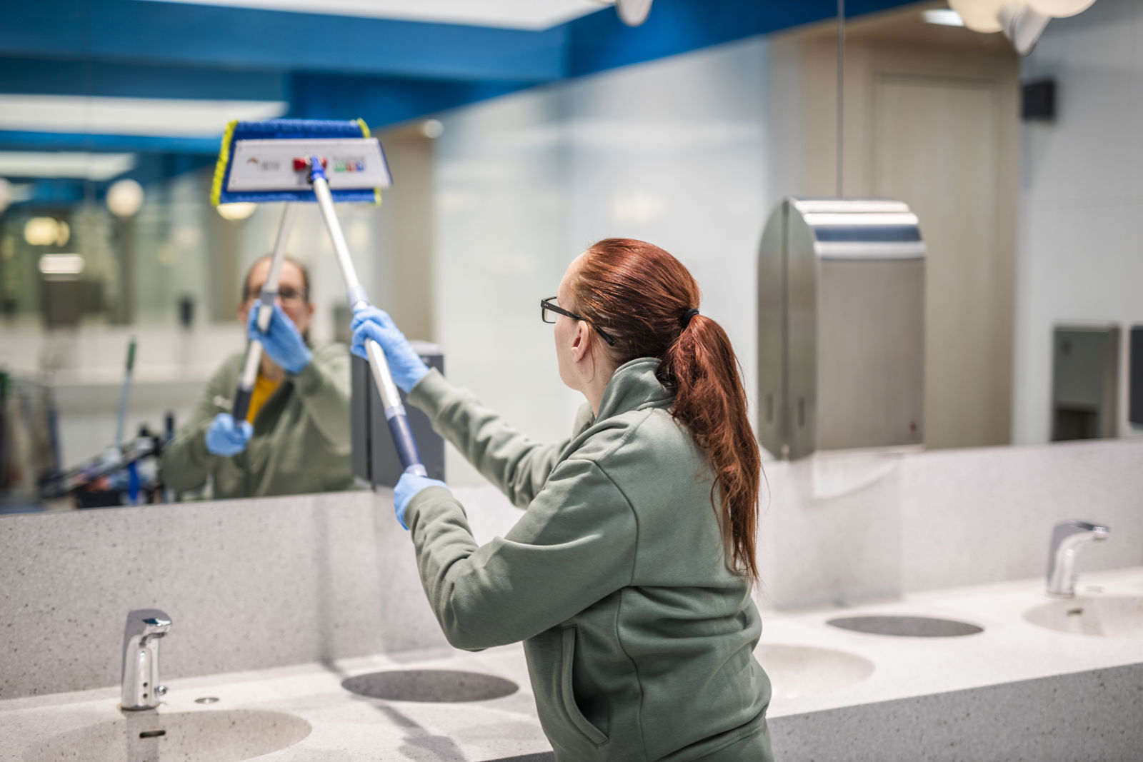 Samhallsmedarbetare rengör en spegel i en toalettmiljö.