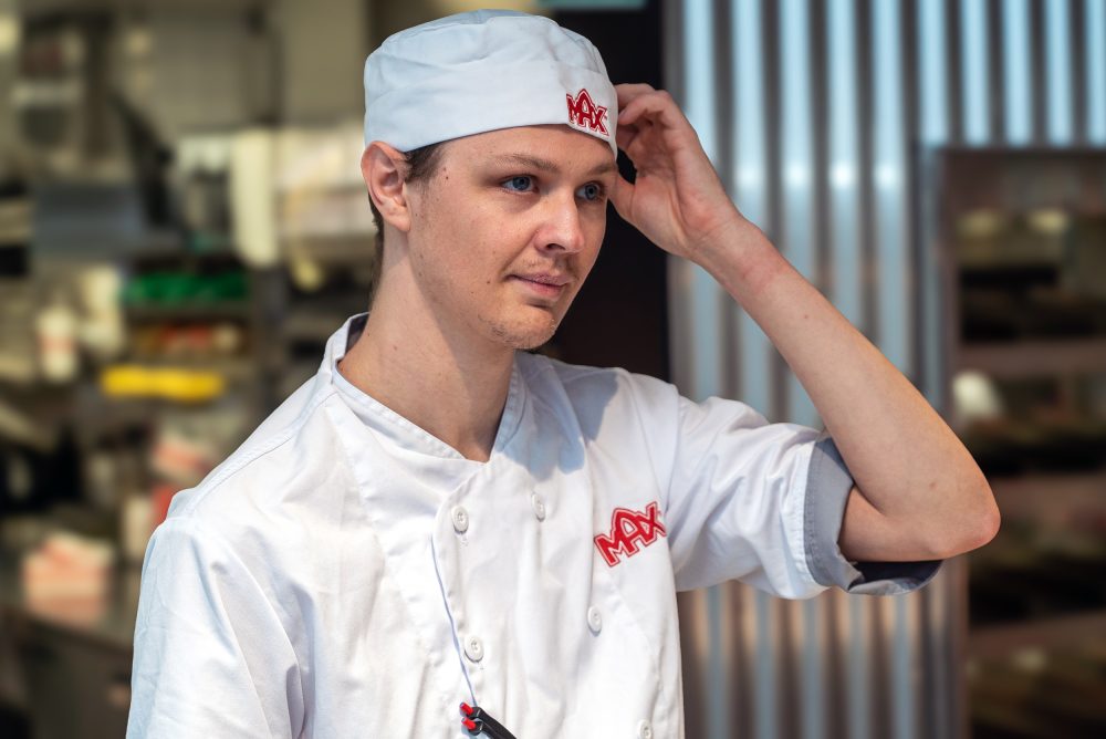 Samhallsmedarbetare arbetar i köket på en Max-restaurang och förbereder mat vid en arbetsstation.