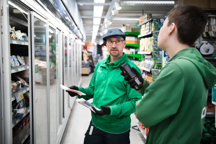 Tony Olaussen fyller på butikskylen tillsammans med Nora Mångsén. De bär gröna arbetskläder. 