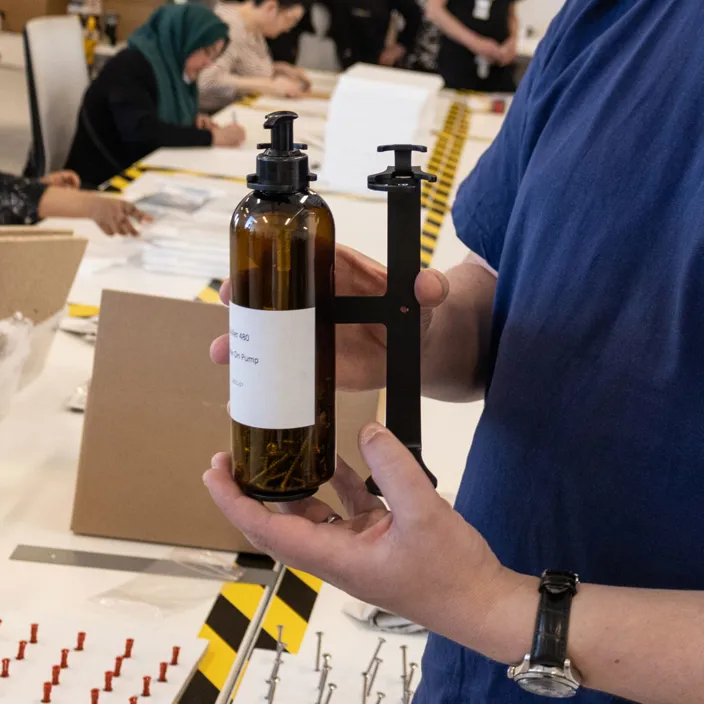 Bild på en hand som håller i tvålpumpen. den har mörkbrun plast och en svart hållare.