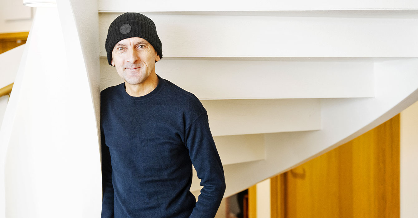 Bild på en man som står i en trappa och litar sig mot en vägg. han har mörka kläder och mössa.