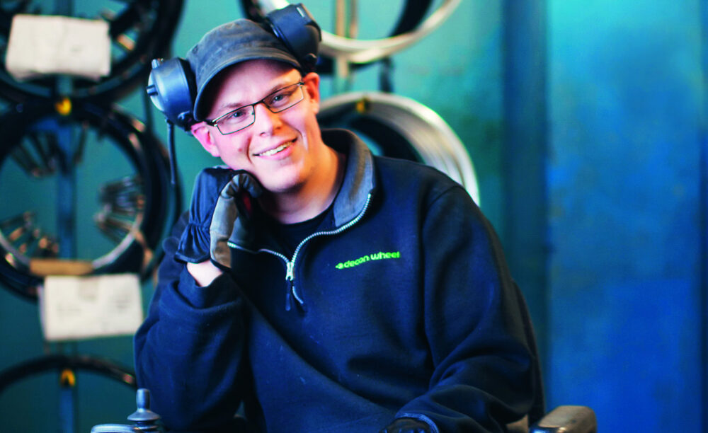 Porträtt på en man med svart keps och glasögon i en arbetsmiljö. Han har hörselkåpor och handskar.