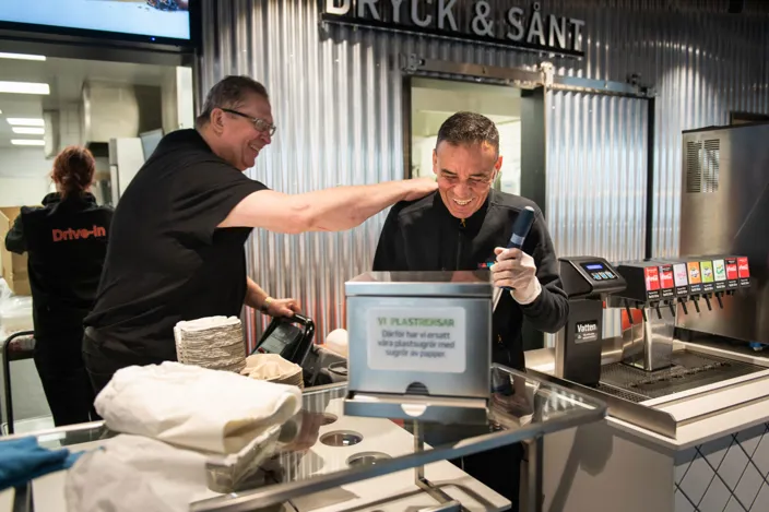 Humberto Rengifo står tillsammans med sin kollega bakom disken på restaurangen. De skrattar båda två.