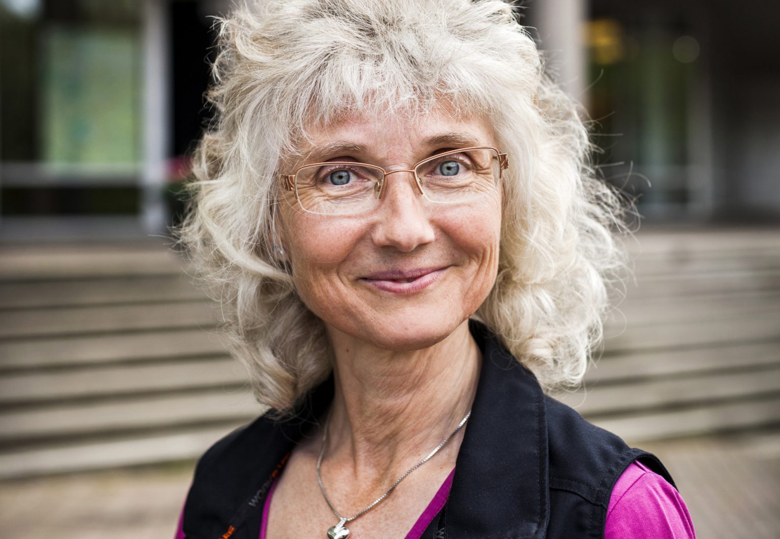 Porträtt av kvinna med glasögon och ljust lockigt hår utomhus.