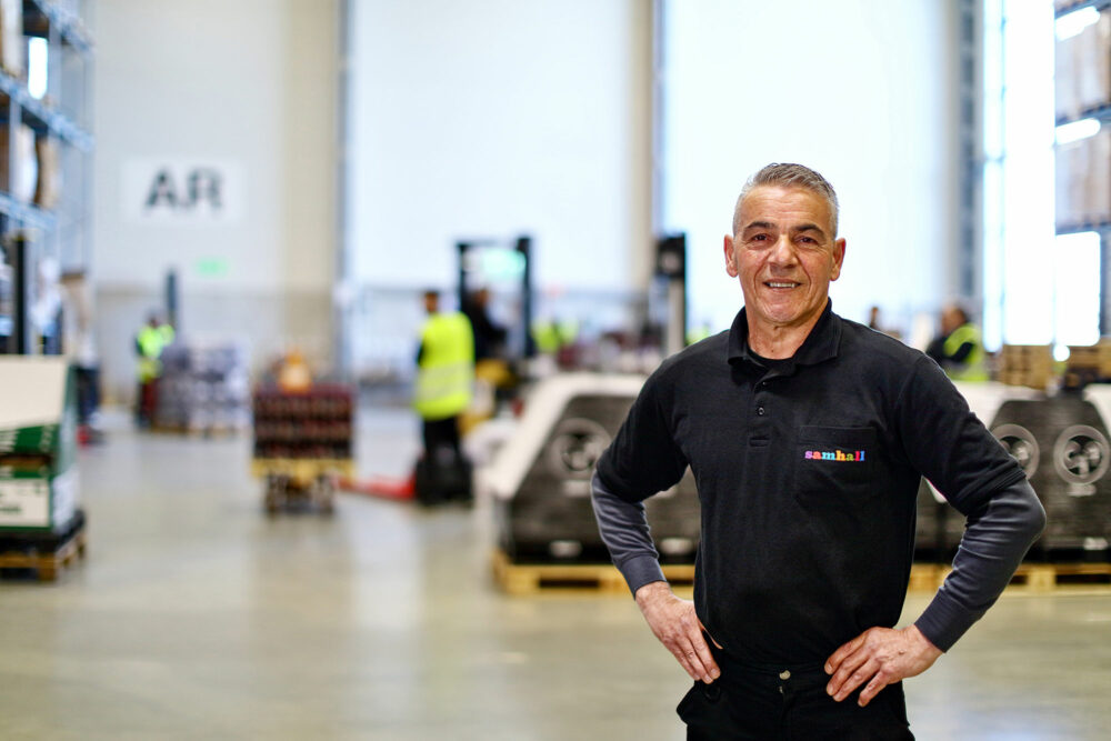 Man som står i lagermiljö. Han har händerna på midjan och ler mot kameran.