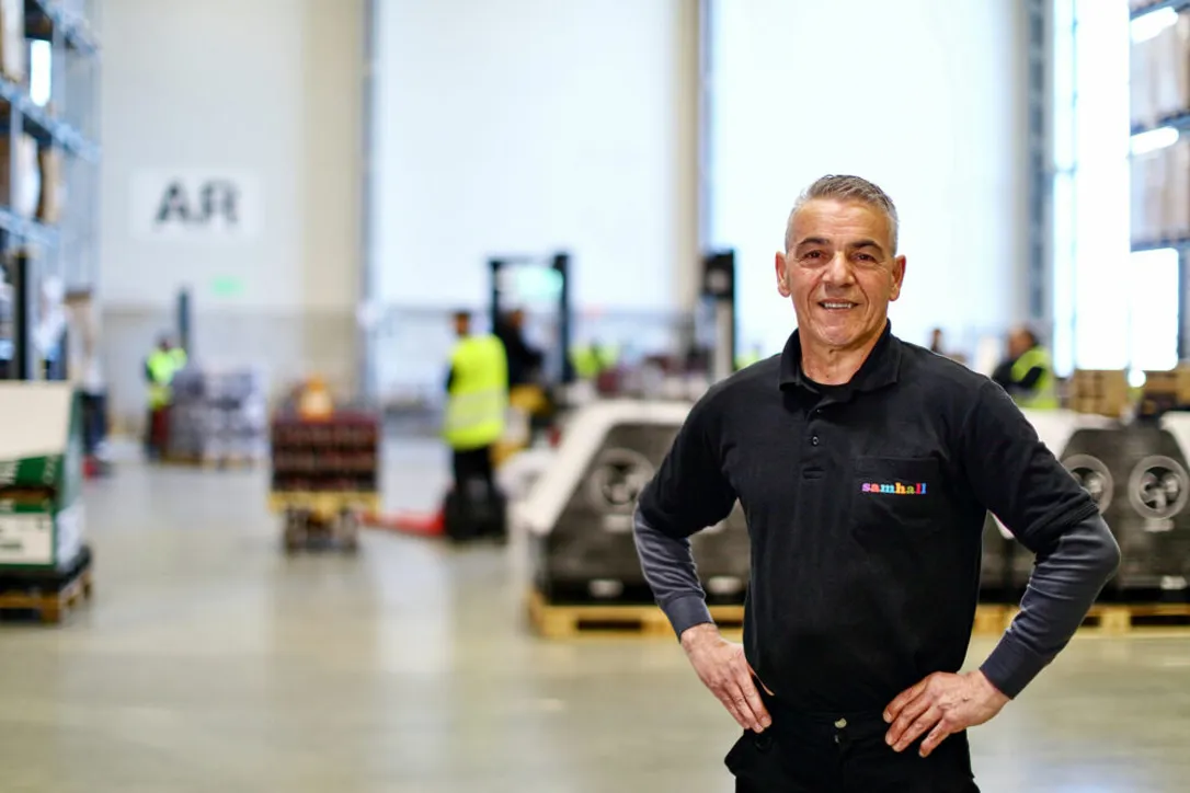 Man som står i lagermiljö. Han har händerna på midjan och ler mot kameran.