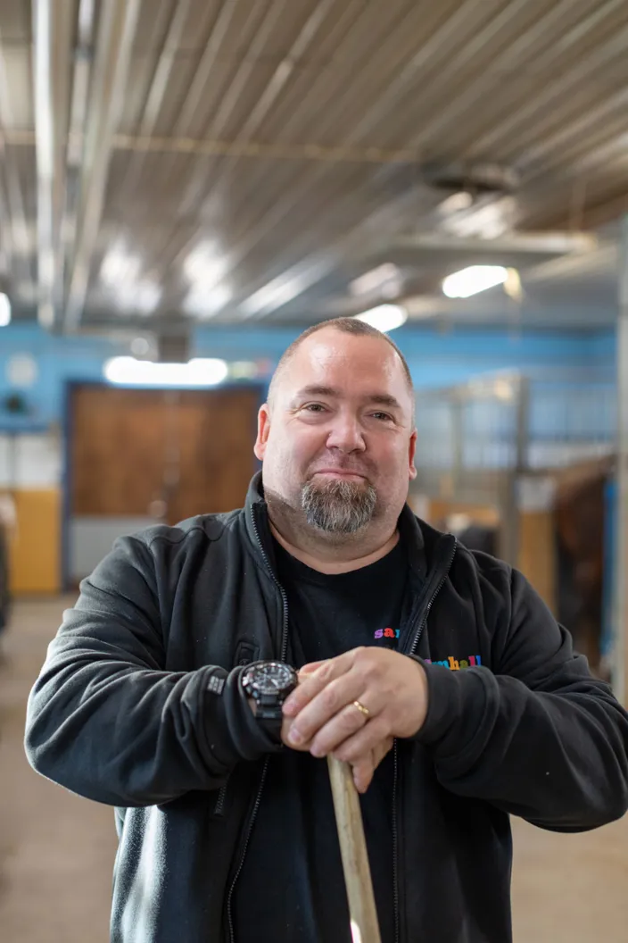 Bild på en man som lutar sig mot ett kvastskaft i ett stall.