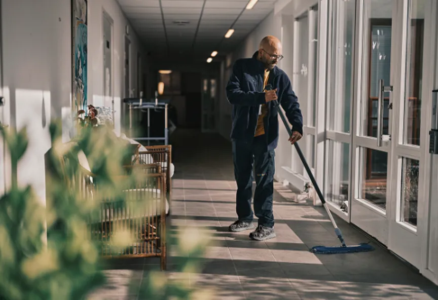 En Samhallmedarbetare moppar golvet i en korridor med stora fönster.
