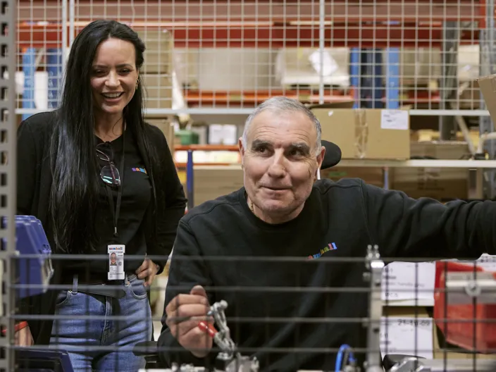 Bild på två samchallmedarbetare i en lagerlokal, en tjej och en kille. Båda bär svarta arbetskläder.