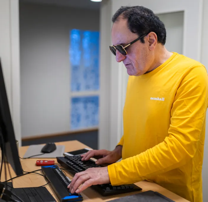 En Samhallmedarbetare använder en dator med hjälpmedel vid ett skrivbord.