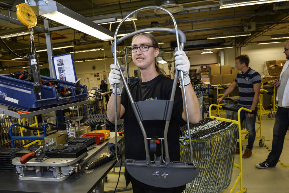 Person med långt hår i hästsvans och glasögon jobbar i ett rum.