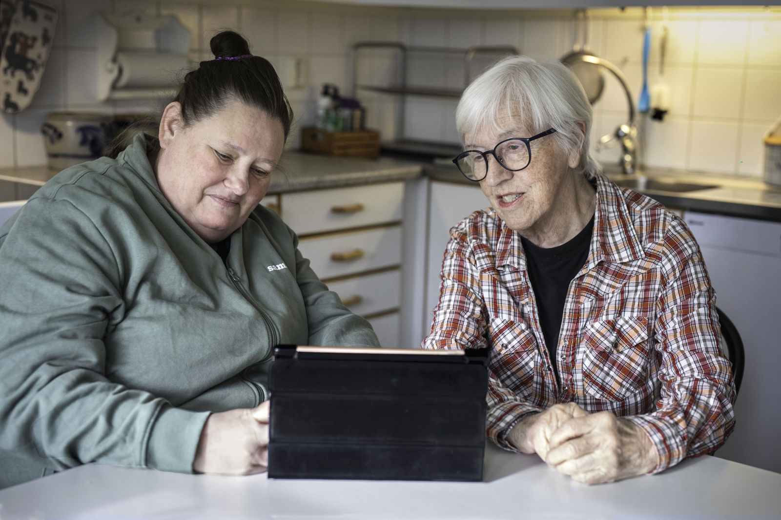 En Samhallanställd och en äldre kvinna tittar på en Ipad. Den Samhallanställda personen tar upp kvinnans matbeställning.