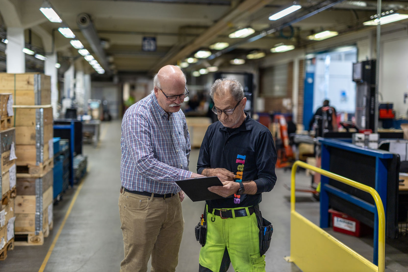 Jan Strandesjö (vänster), hållbarhetschef, Beslag och Metall, och Abdula Mustafa, teamleader Samhall. på Beslag och Metall i Vetlanda. Jan har glasögon och blårutig skjorta. Abdula håller i en dokumenthållare och har glasögon och mörkblå Samhall-skjorta.