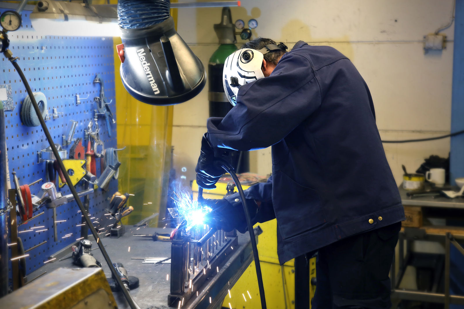En samhallsanställd svetsar en metallbit i en verkstad.